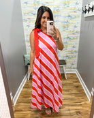 Woman taking a mirror selfie wearing a red and pink striped dress in a room with a patterned wall.