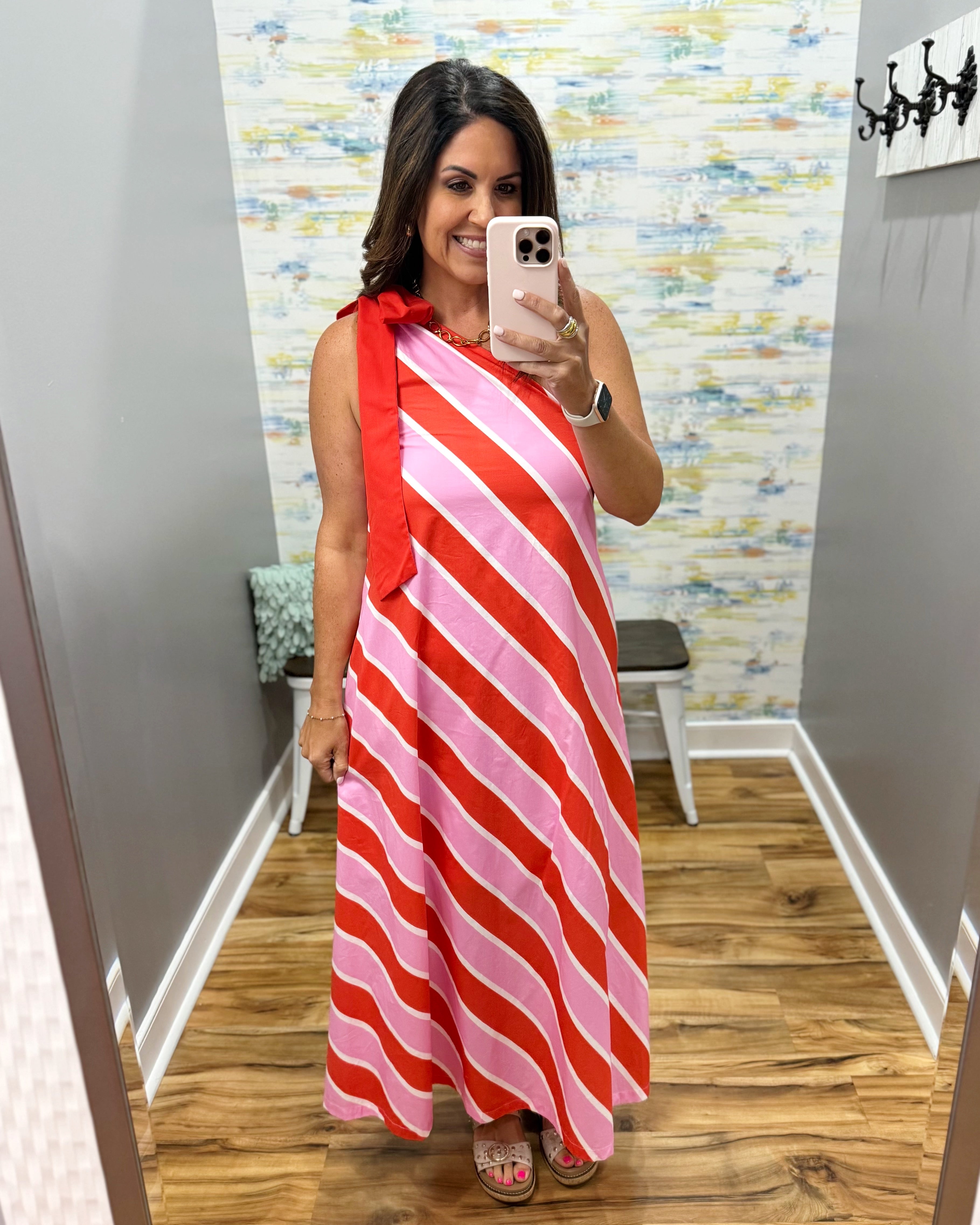 Woman taking a mirror selfie wearing a red and pink striped dress in a room with a patterned wall.