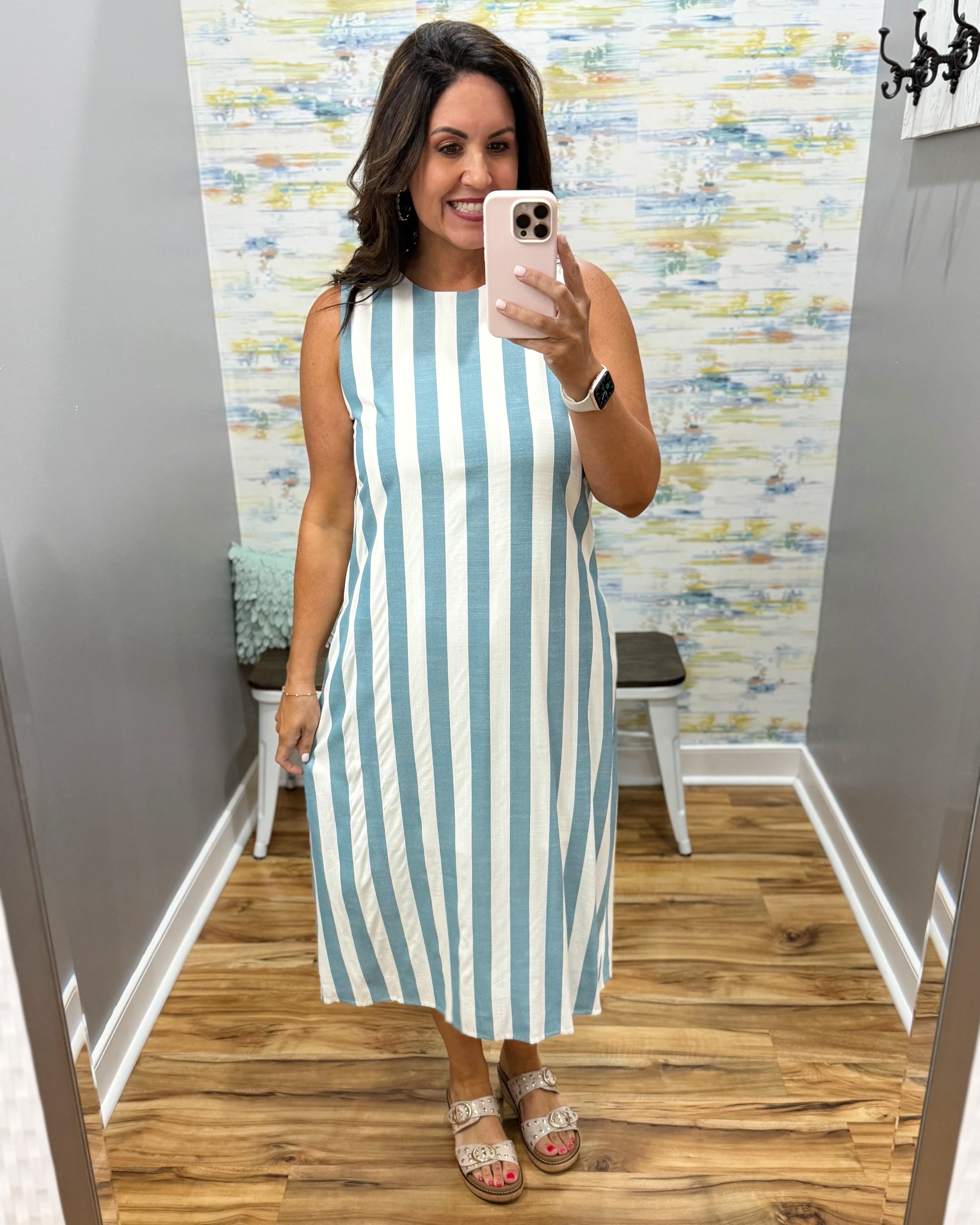 Woman taking a mirror selfie wearing a blue and white striped dress in a room with a patterned wall.