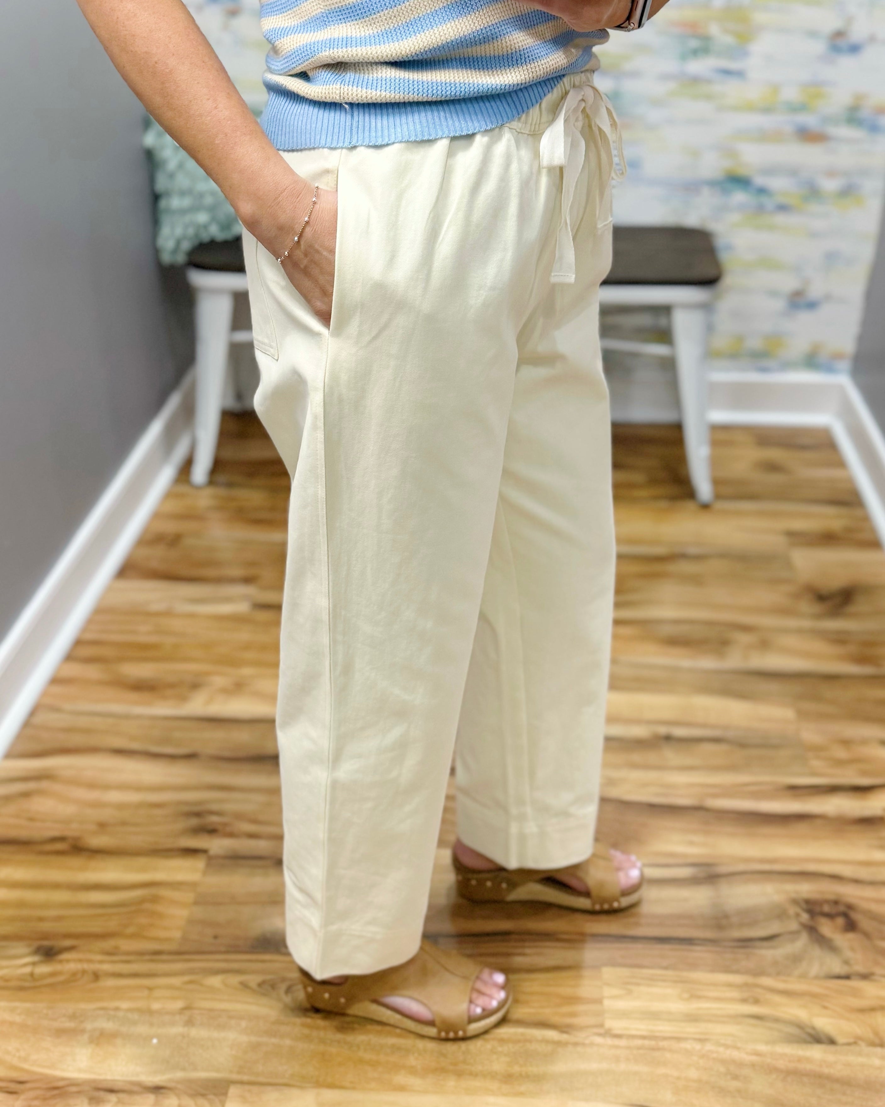 Person wearing light-colored pants and a striped shirt on a wooden floor.