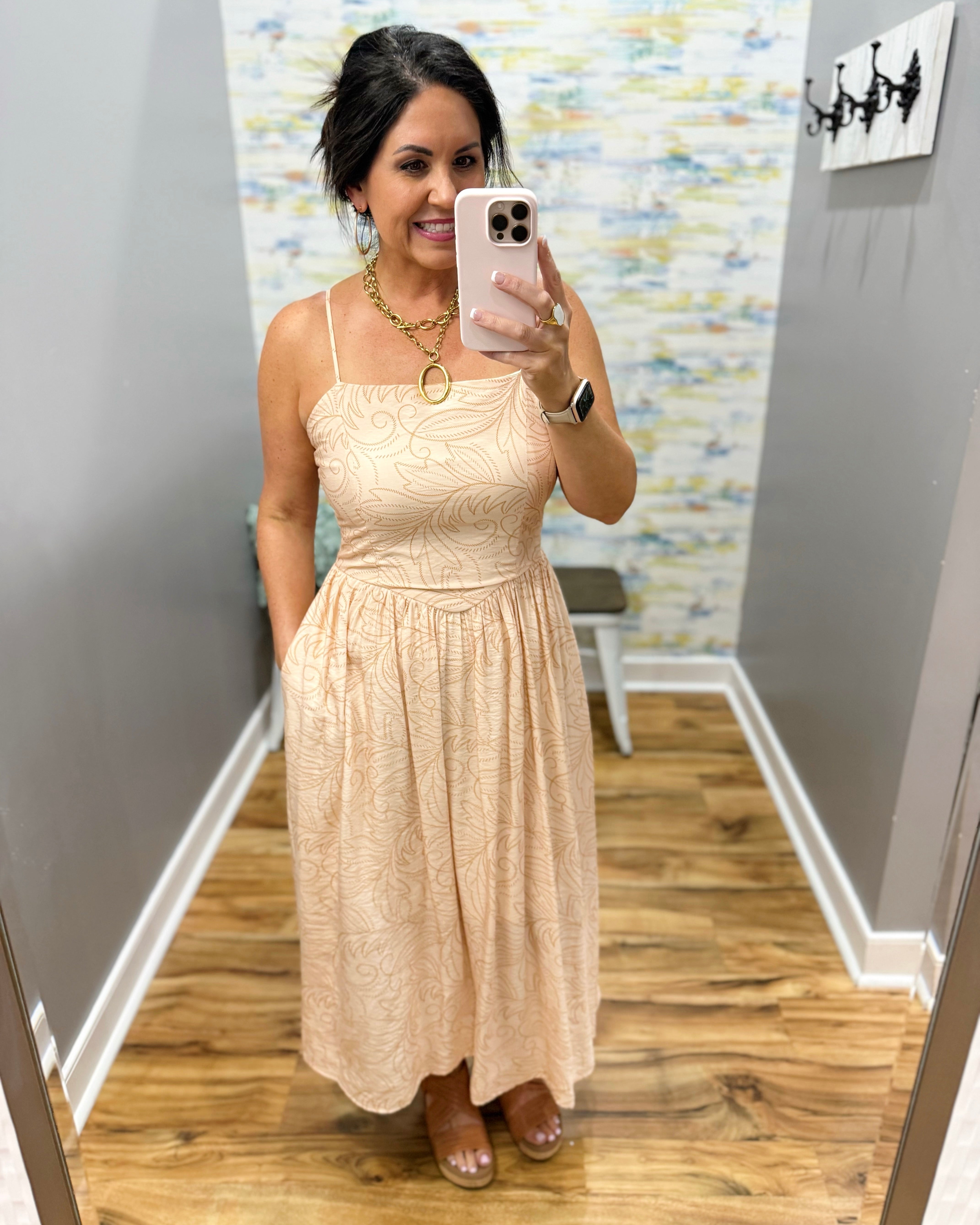 Woman taking a mirror selfie wearing a beige dress in a room with a textured wall.