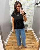 Woman taking a mirror selfie wearing a black top and blue jeans in a room with a colorful wall.