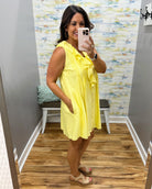 Woman wearing a yellow dress taking a mirror selfie in a room with a patterned wall.