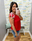 Woman taking a mirror selfie wearing a red top with white accents and denim shorts in a room with a colorful wall.