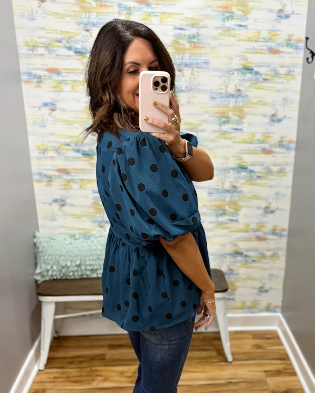 woman taking a selfie wearing a teal top with black polka dots and puff sleeves.