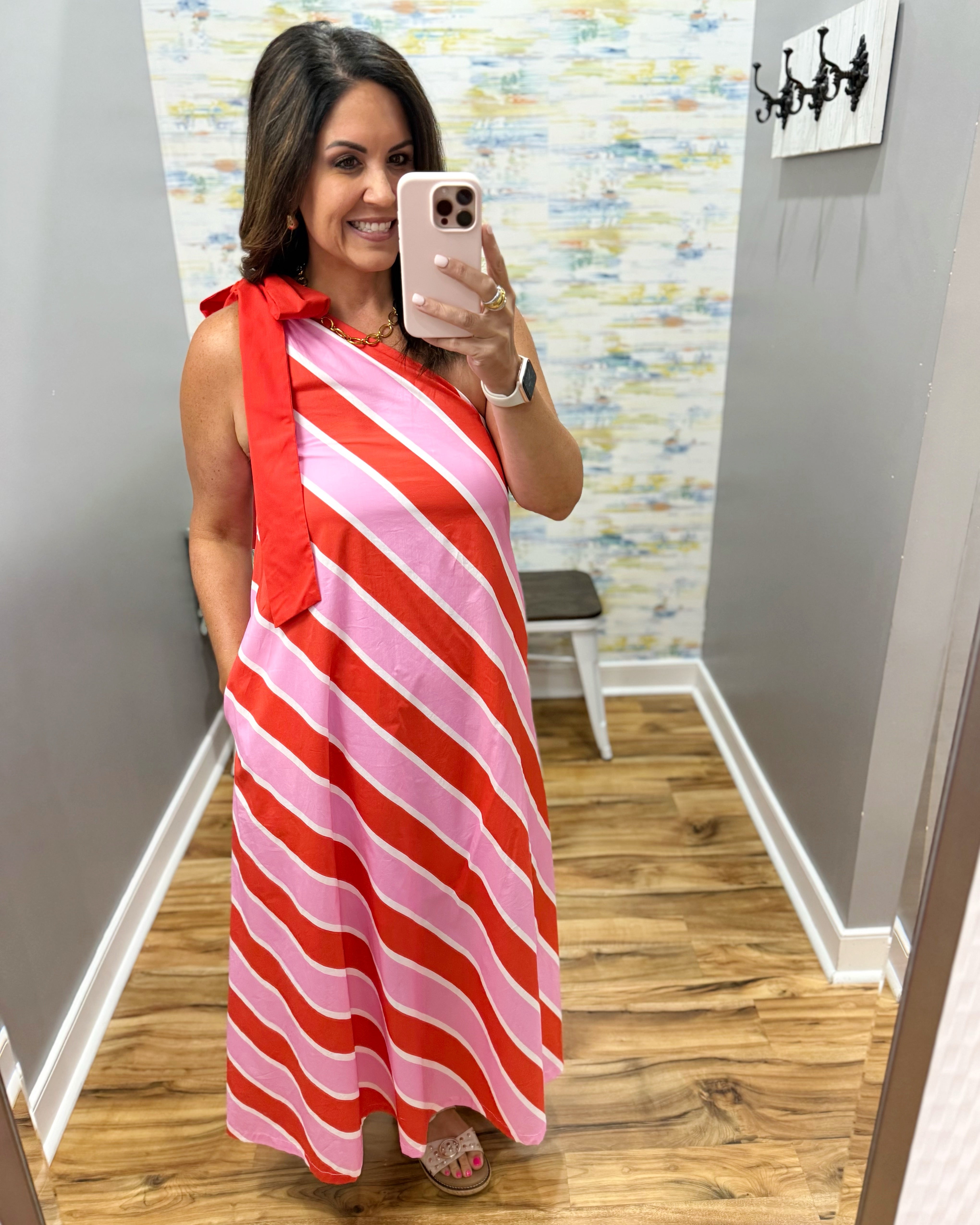Woman taking a mirror selfie wearing a red and pink striped dress in a room with a patterned wall.