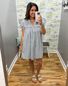 Woman taking a mirror selfie wearing a striped dress in a room with a colorful wall.