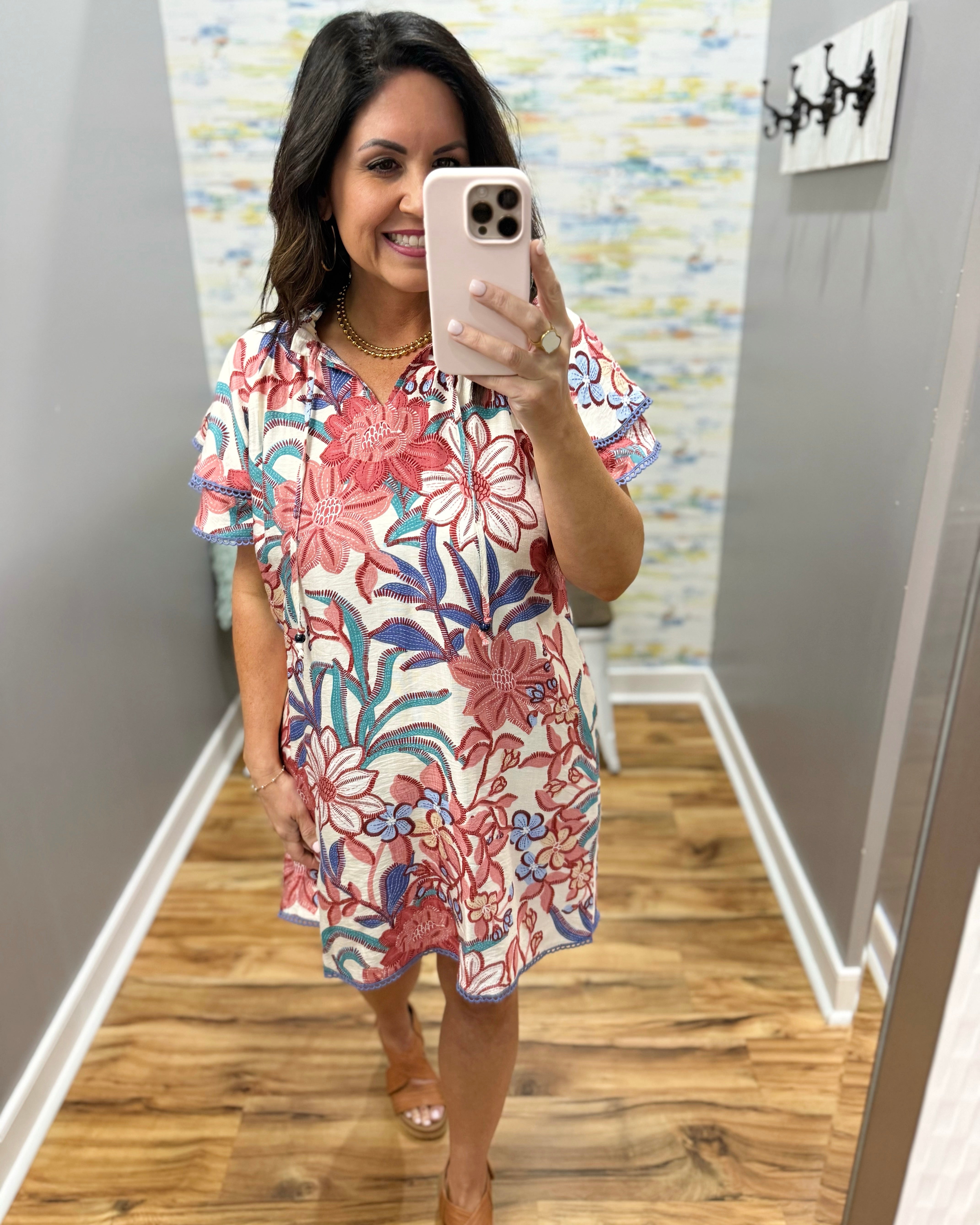 Woman taking a mirror selfie wearing a floral dress in a room with a colorful wall.