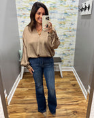 A woman takes a mirror selfie in a fitting room wearing a beige satin blouse with puff sleeves and dark blue flare jeans.