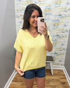 Woman taking a mirror selfie wearing a yellow shirt and denim shorts in a room with a colorful wall.