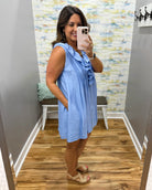 Woman taking a mirror selfie wearing a blue dress in a room with a patterned wall.