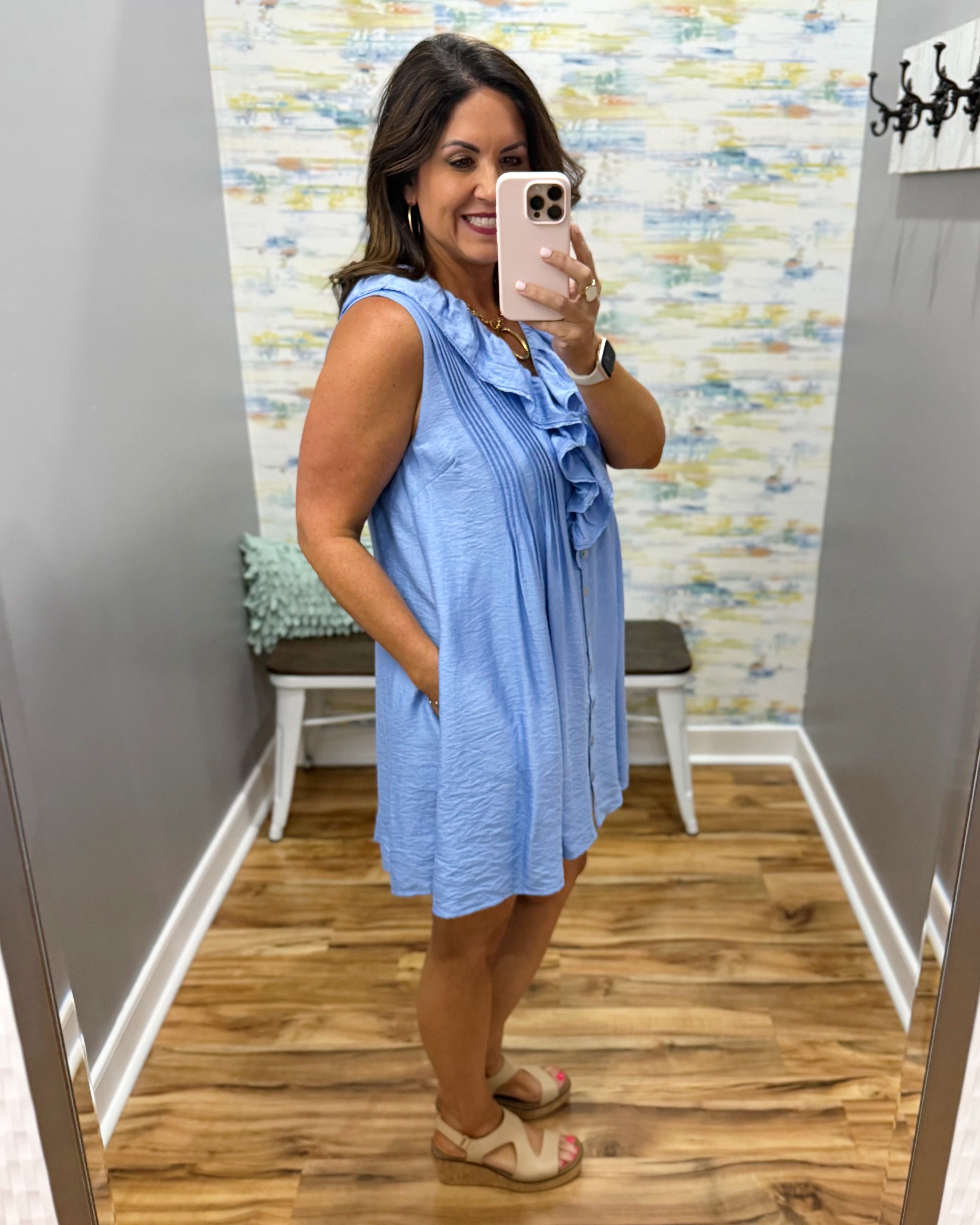 Woman taking a mirror selfie wearing a blue dress in a room with a patterned wall.