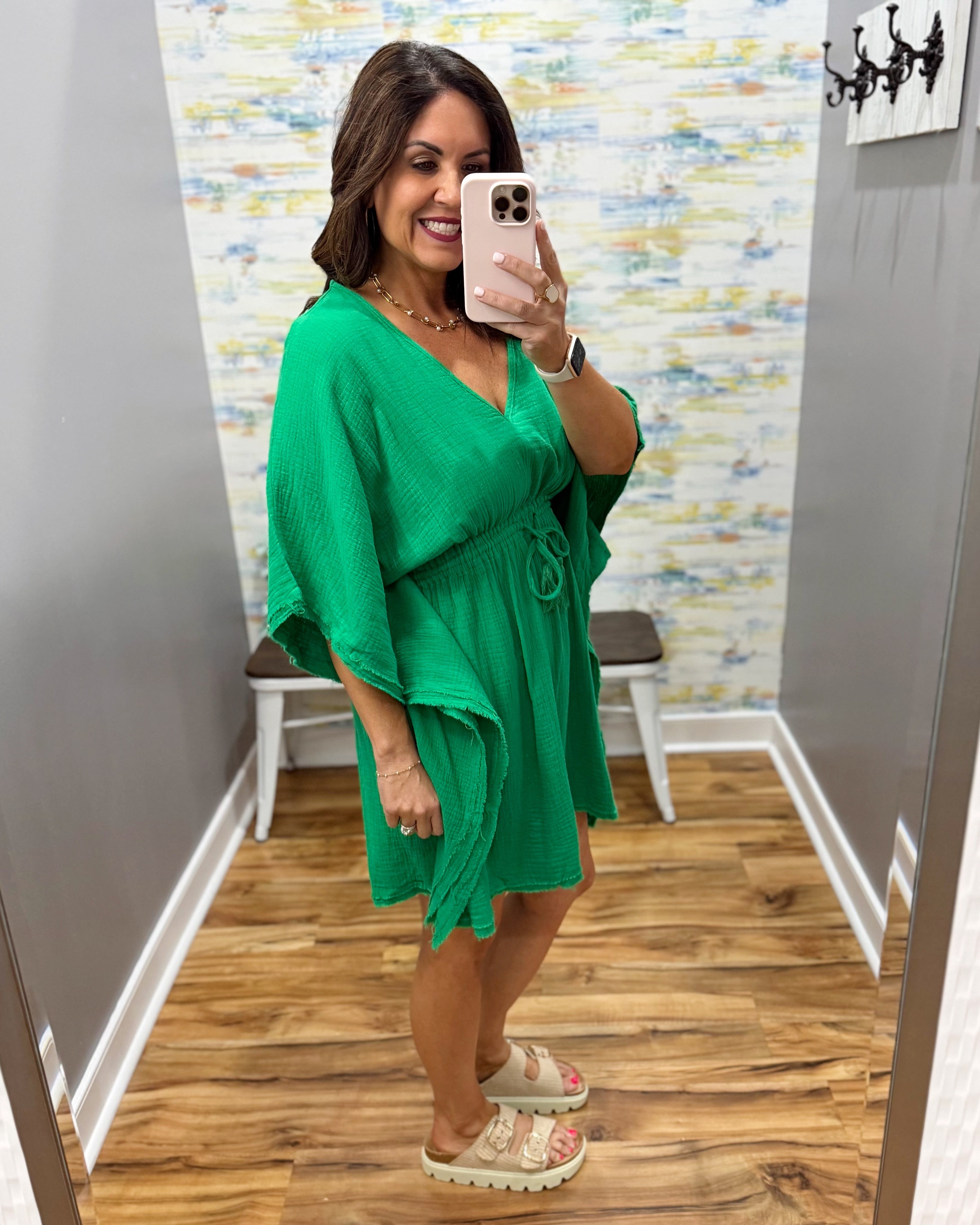 Woman taking a mirror selfie wearing a green dress in a room with a colorful wall.
