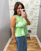 Woman taking a mirror selfie wearing a green floral top and blue jeans in a room with a colorful wall.