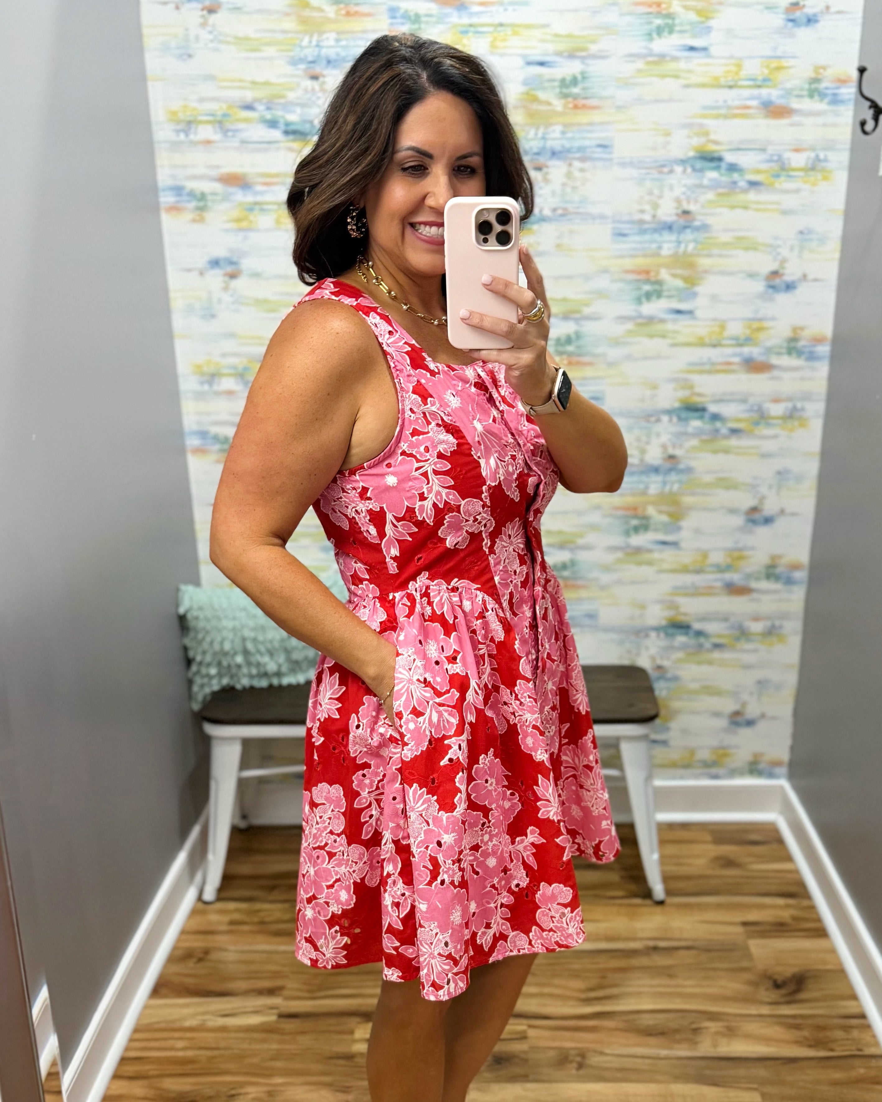 Woman taking a mirror selfie wearing a red floral dress in a room with a colorful wall.