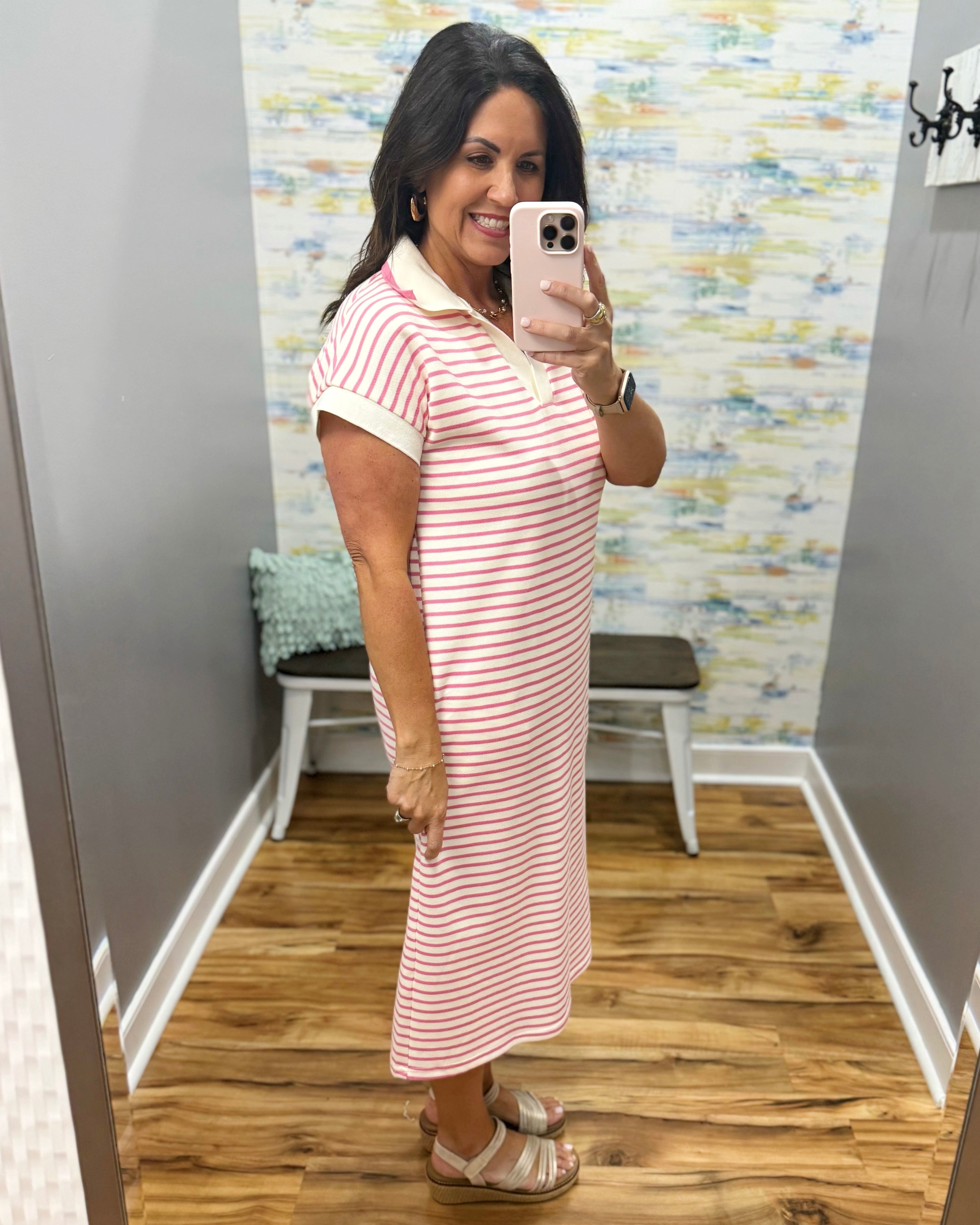 Woman taking a mirror selfie wearing a pink and white striped dress in a fitting room.