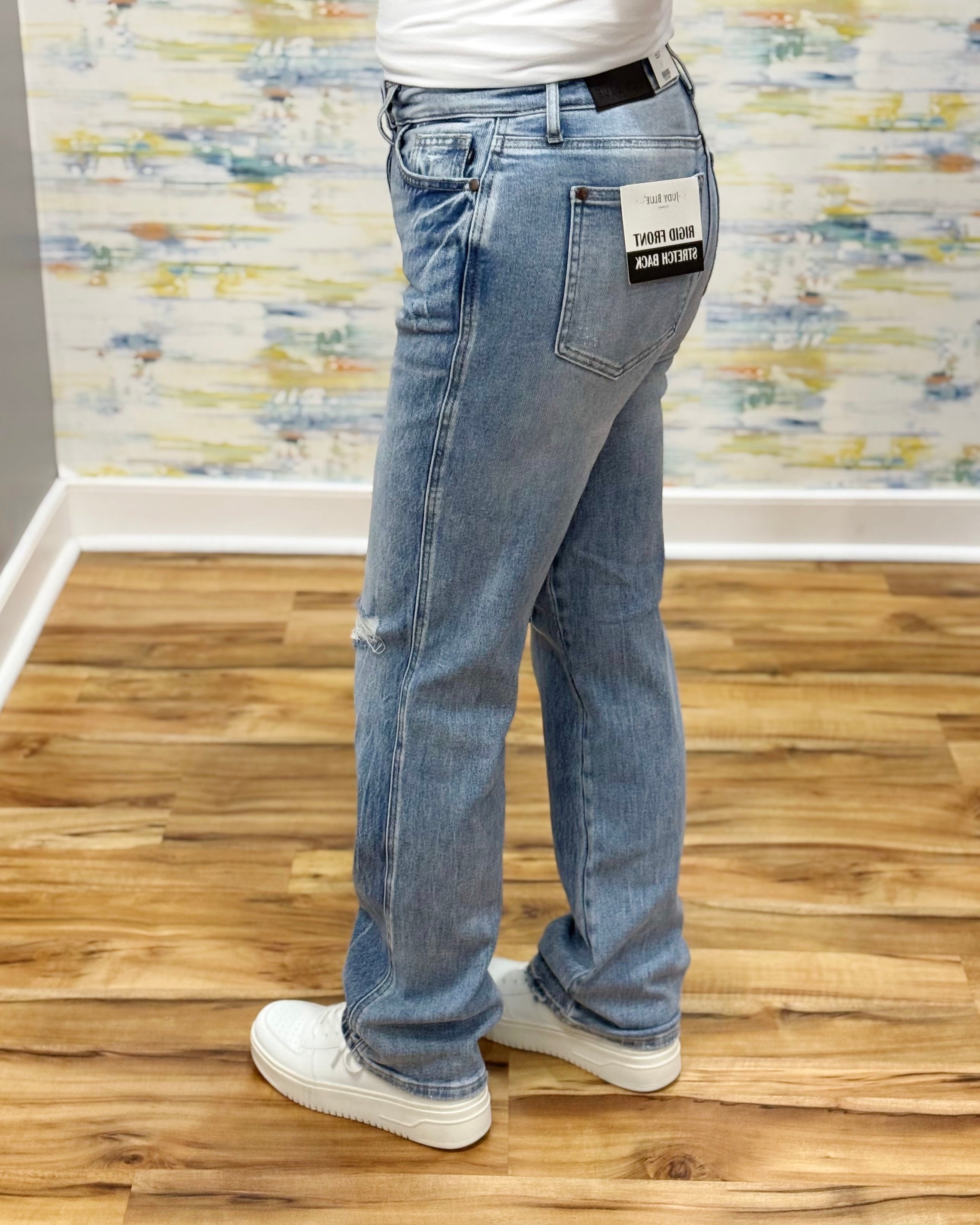 Person wearing light blue jeans with a visible brand label on a wooden floor.