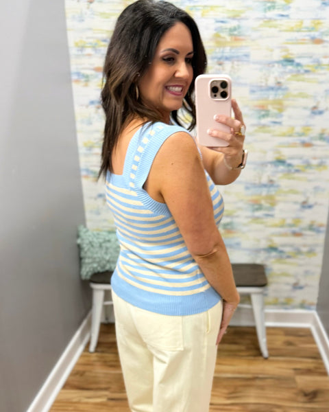 Woman wearing a blue and yellow striped sleeveless top and white pants.