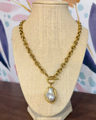 Chansuttpearls Pearl Drop necklace with a large irregular white pearl pendant, displayed on a beige fabric jewelry bust against a colorful floral background.