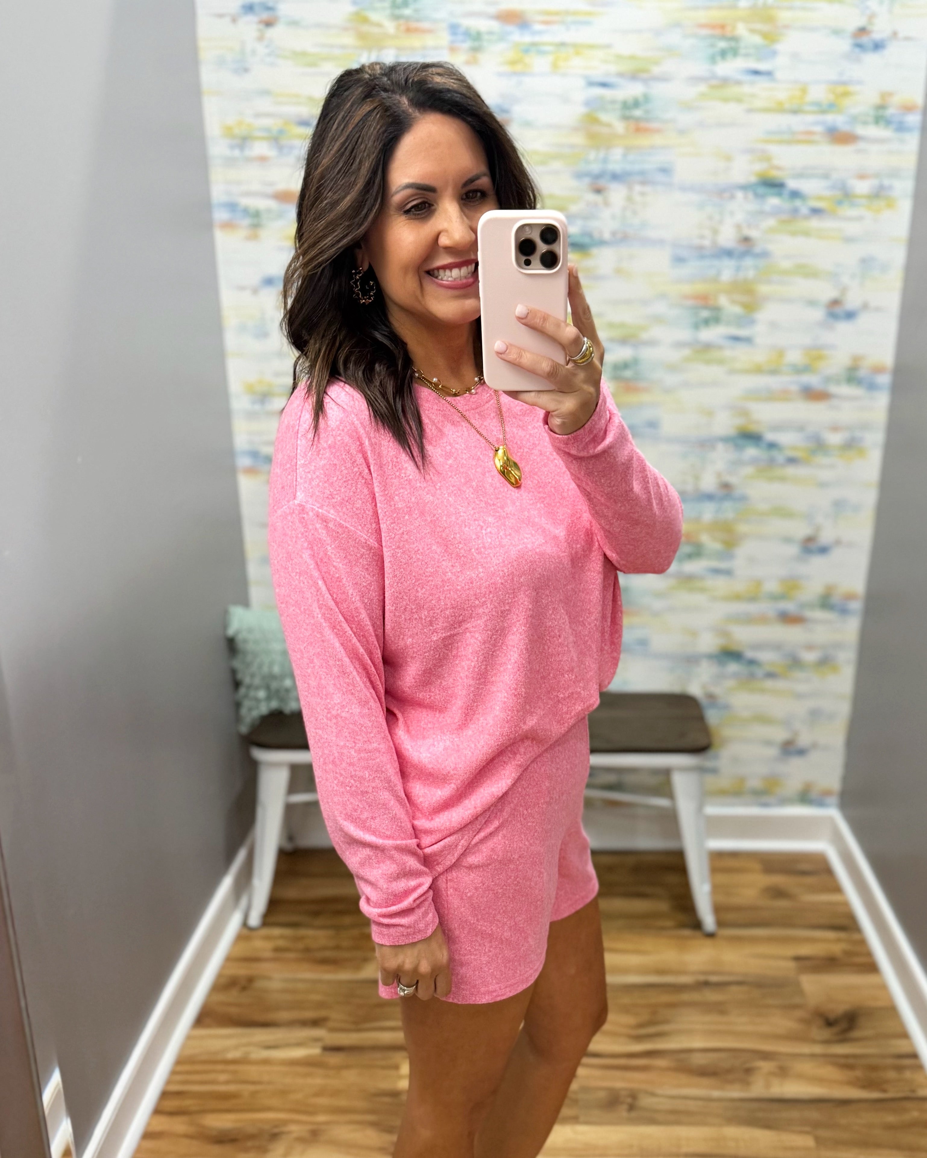 Woman taking a mirror selfie wearing a pink outfit in a room with a colorful wall.