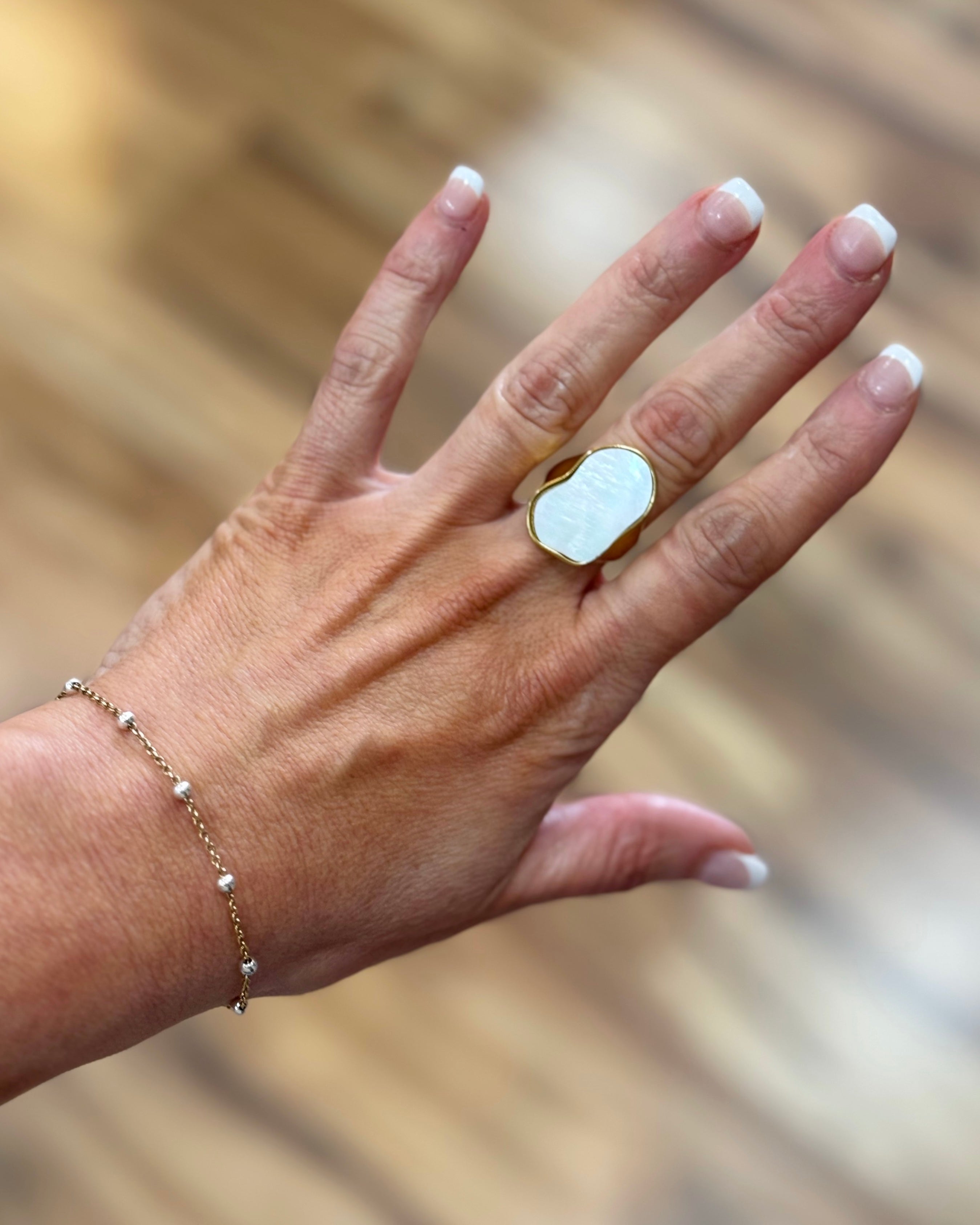 Hand wearing a gold ring with a white stone against a blurred natural background