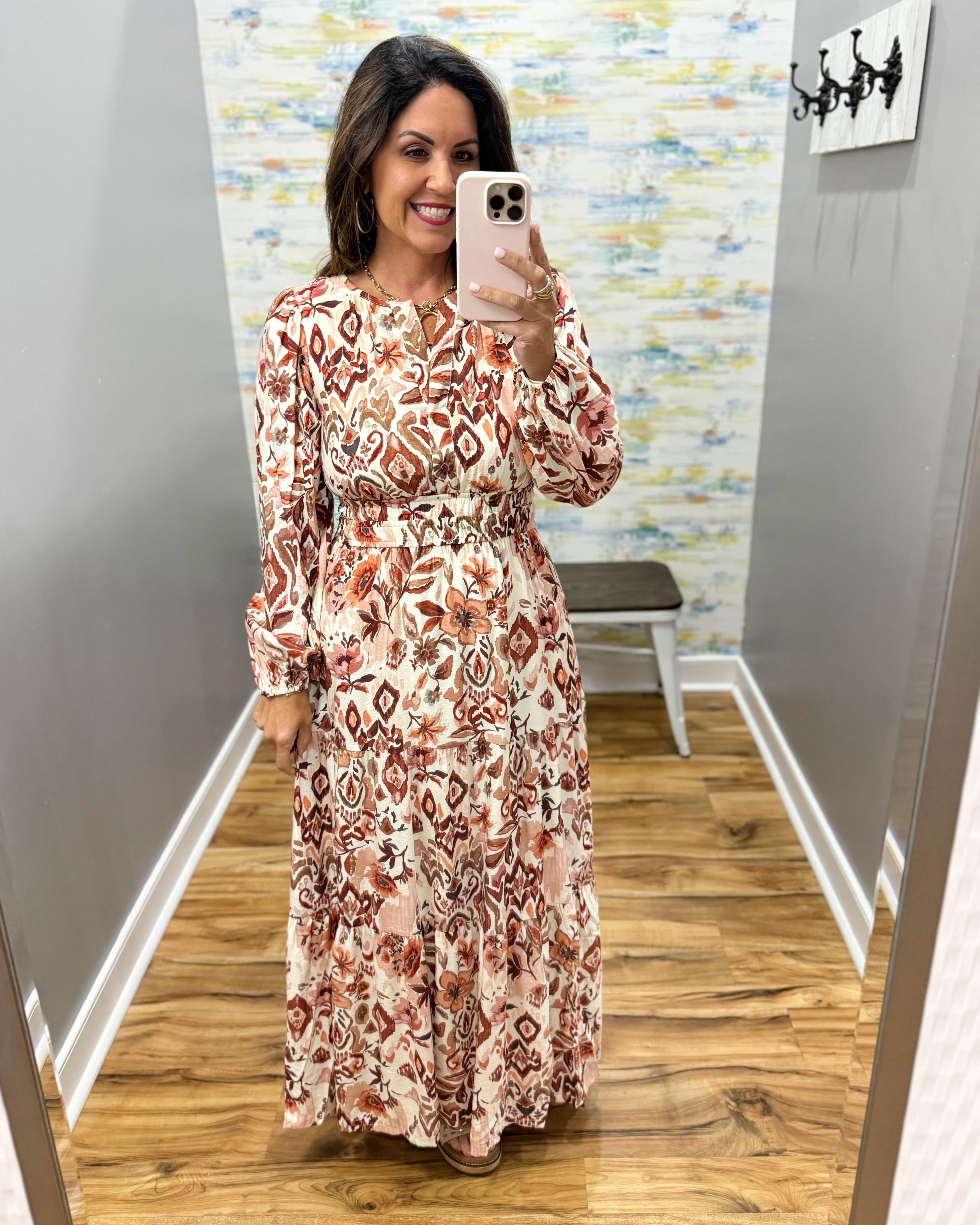A woman takes a mirror selfie in a fitting room wearing a long-sleeve maxi dress with a rust, brown, and cream geometric ikat pattern.