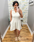 Woman taking a mirror selfie wearing a white dress in a room with a colorful wall.