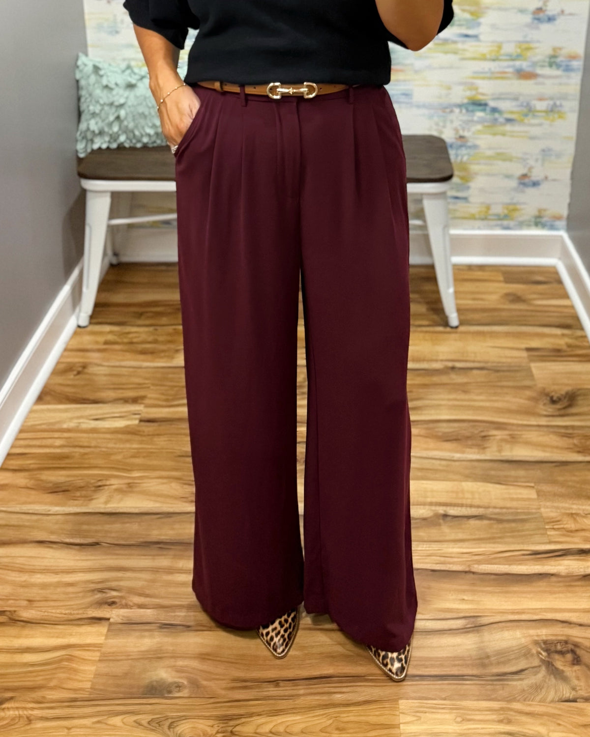 A woman takes a mirror selfie in a fitting room wearing a black short-sleeve sweater and high-waisted wide-leg pants in merlot with Corkys Sober Up shoes in leopard.