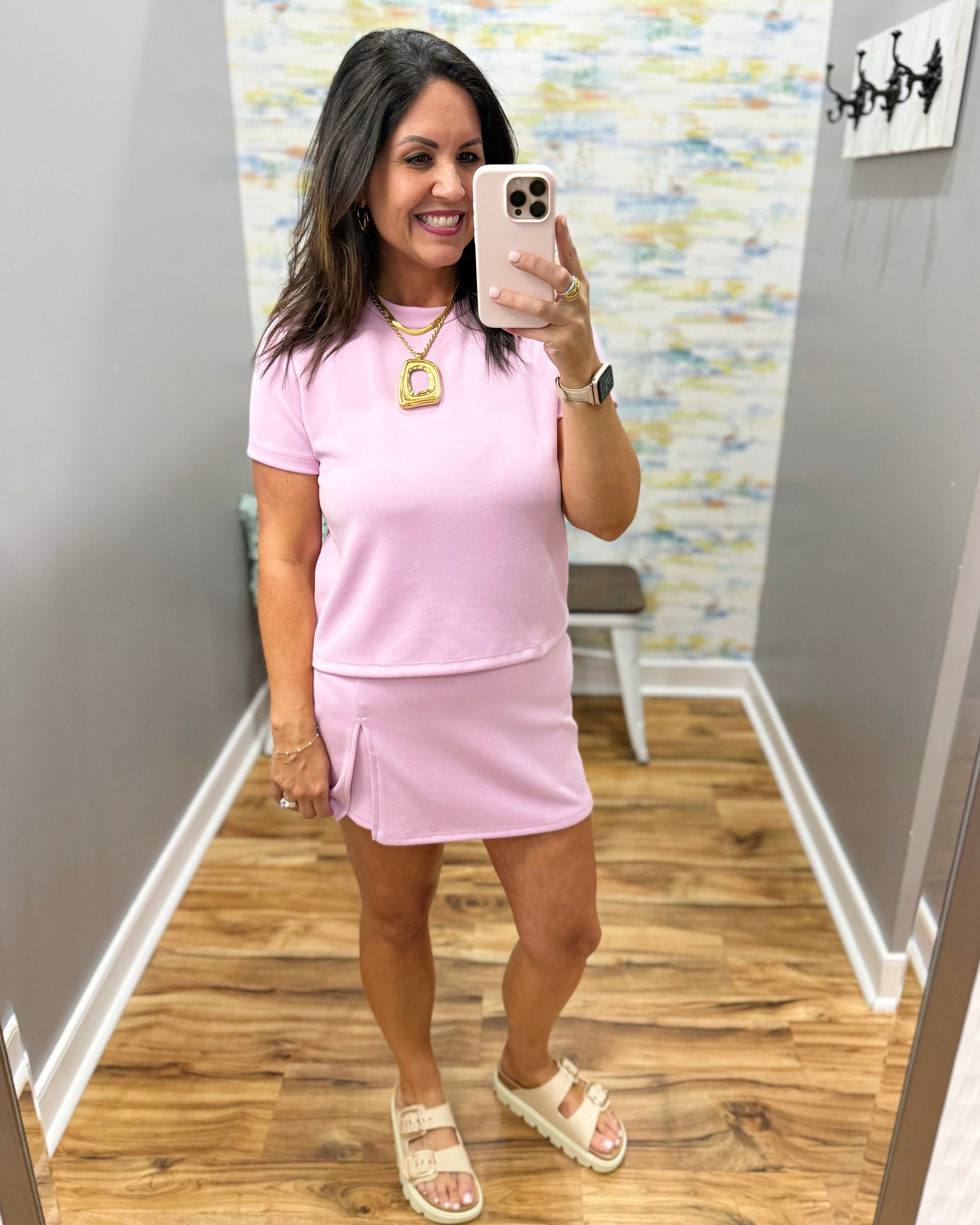 Woman taking a mirror selfie wearing a pink outfit in a room with a colorful wall.