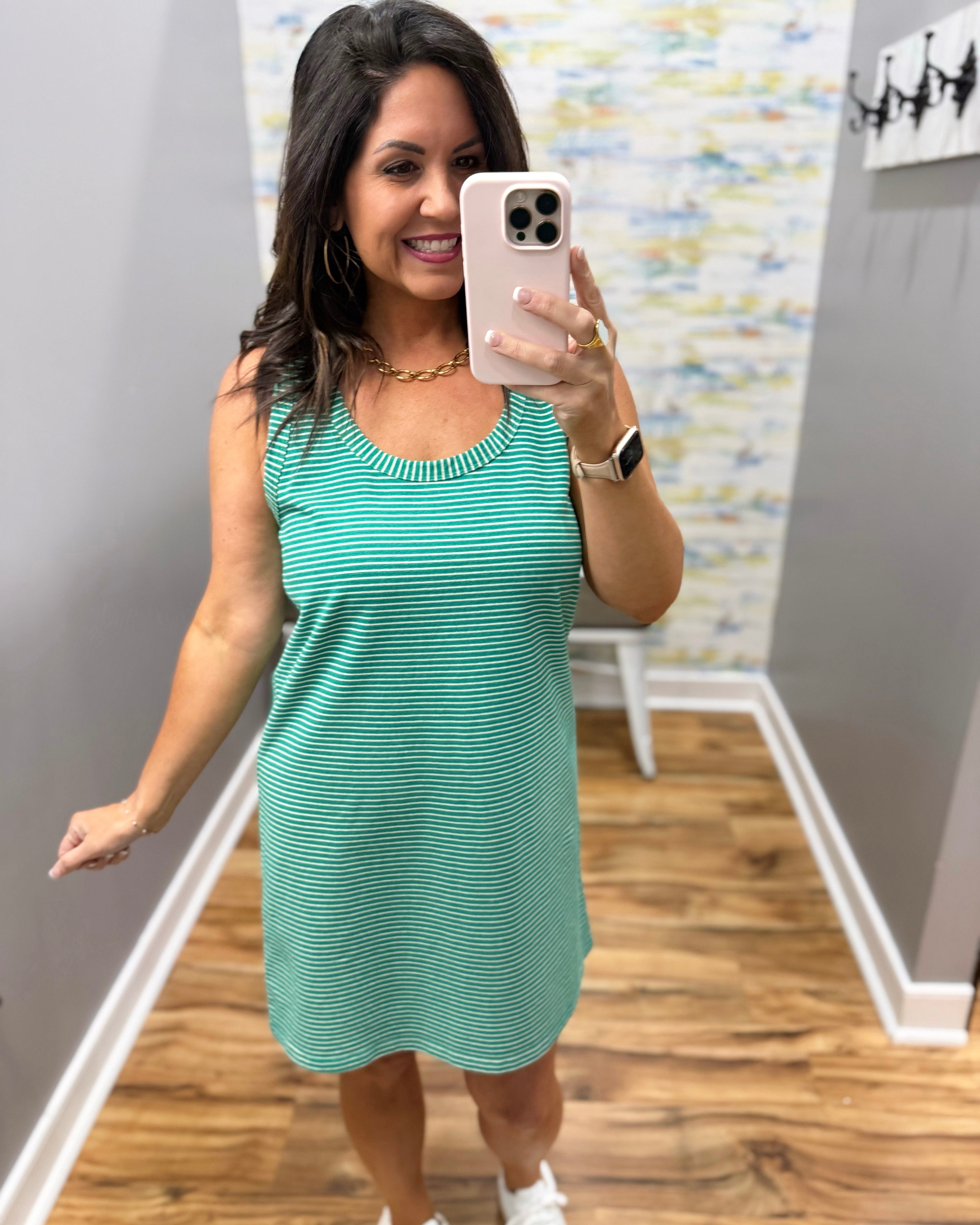 Woman taking a mirror selfie wearing a green striped dress in a room with a patterned wall.