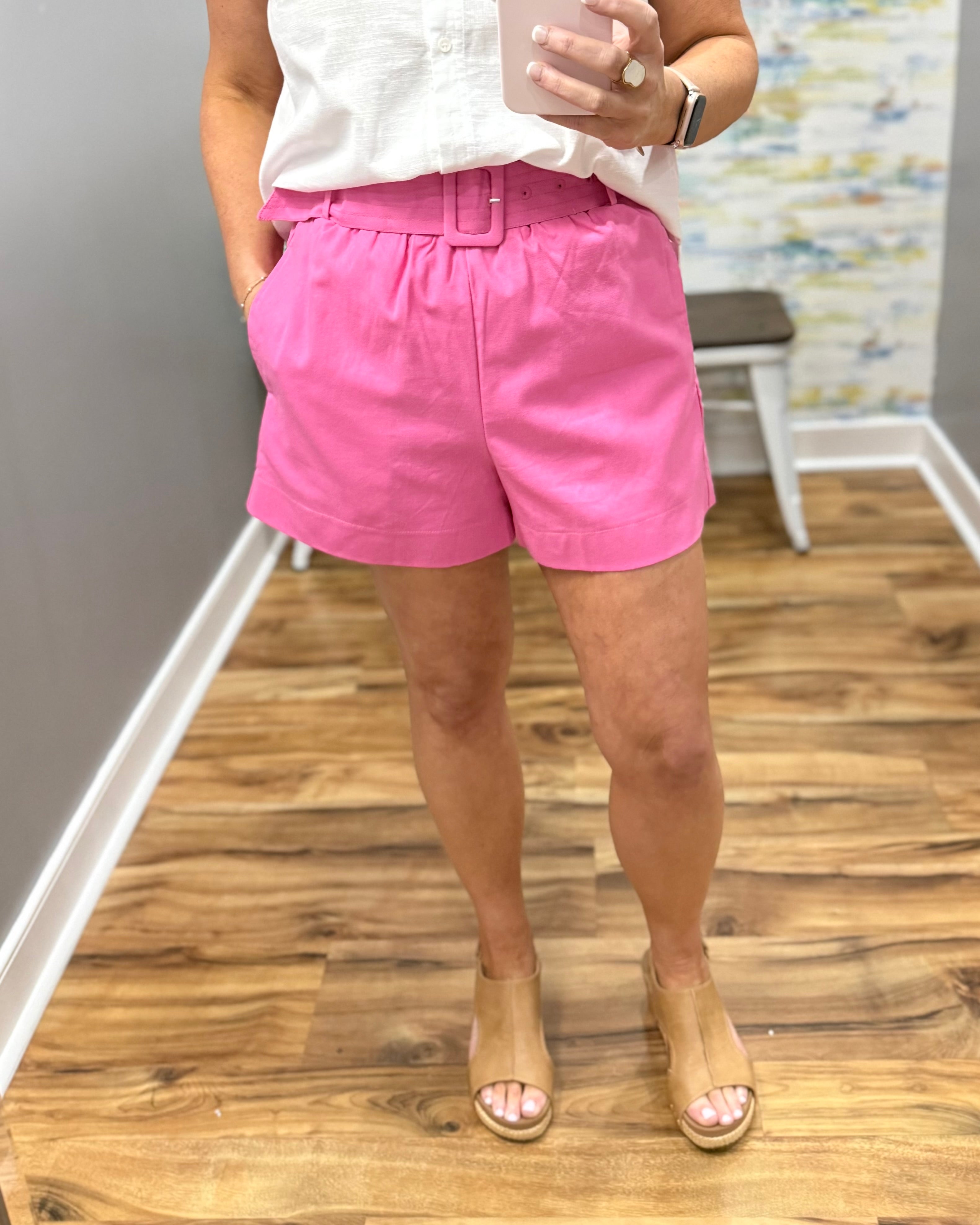 Person wearing pink shorts and a white top on a wooden floor.
