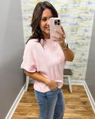Woman taking a mirror selfie wearing a pink sweater and blue jeans in a room with a colorful wall.