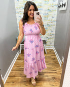 Woman taking a mirror selfie wearing a pink dress with floral patterns in a room with a textured wall.