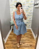 Woman taking a mirror selfie wearing a light blue denim dress in a room with a patterned wall.