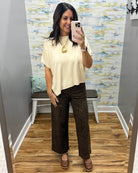 A woman takes a mirror selfie in a fitting room wearing a cream short-sleeve top and brown leopard-print wide-leg pants.