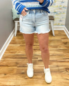 Person wearing a blue and white striped sweater, light denim shorts, and white sneakers on a wooden floor.