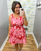 Woman taking a mirror selfie wearing a red floral dress in a room with a colorful wall.