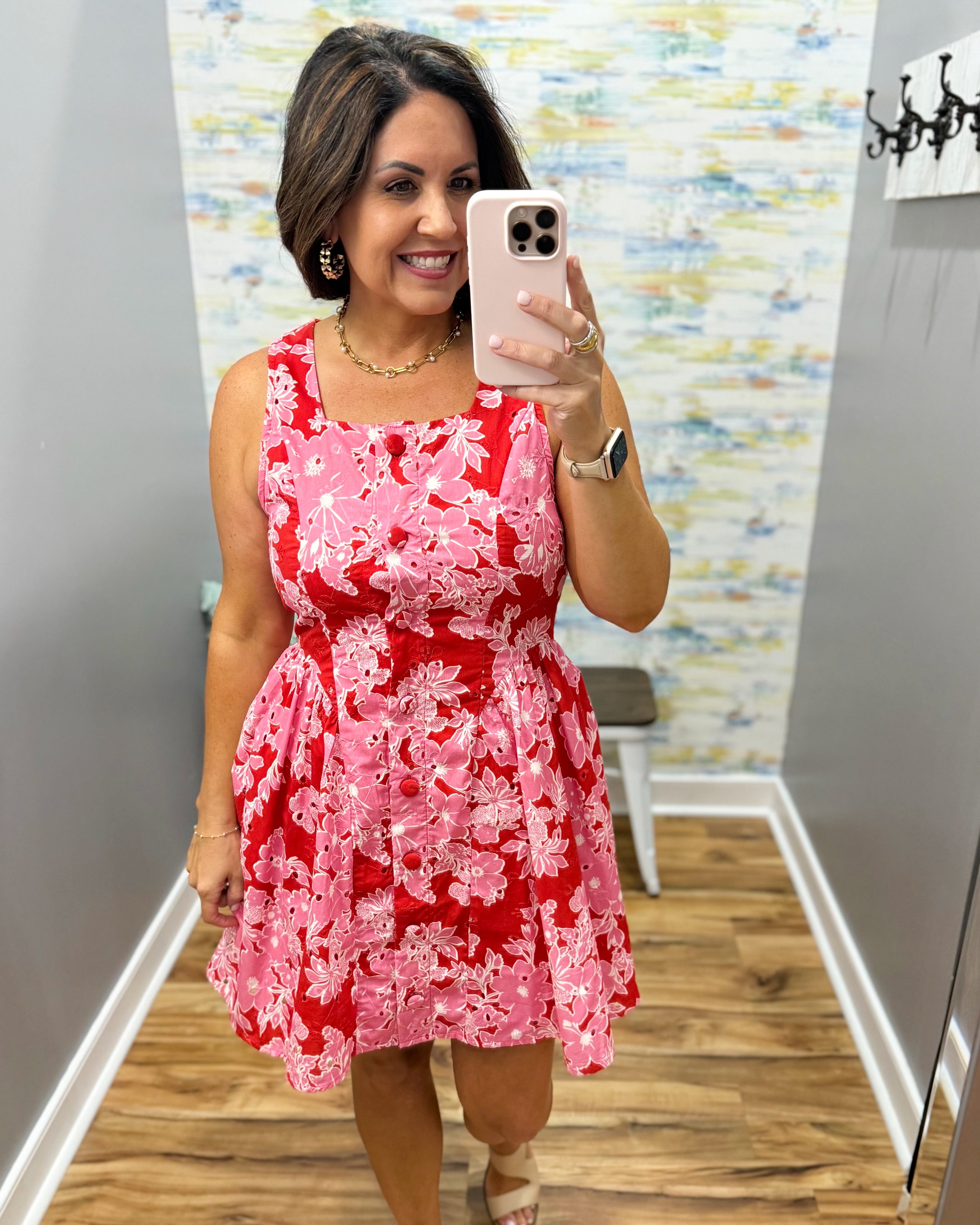 Woman taking a mirror selfie wearing a red floral dress in a room with a colorful wall.