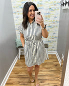Woman wearing a black and white striped dress in a room with patterned wallpaper.