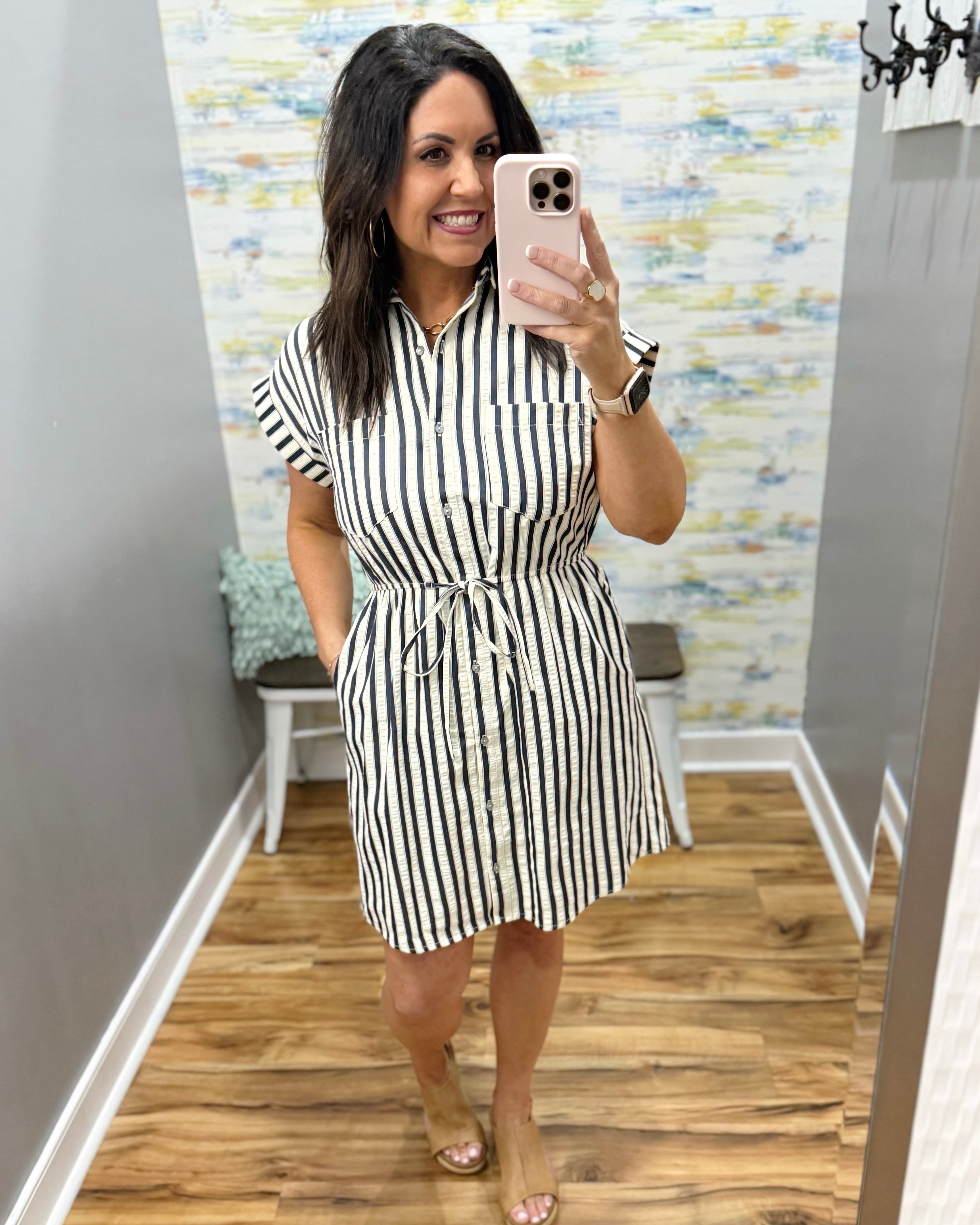 Woman wearing a black and white striped dress in a room with patterned wallpaper.