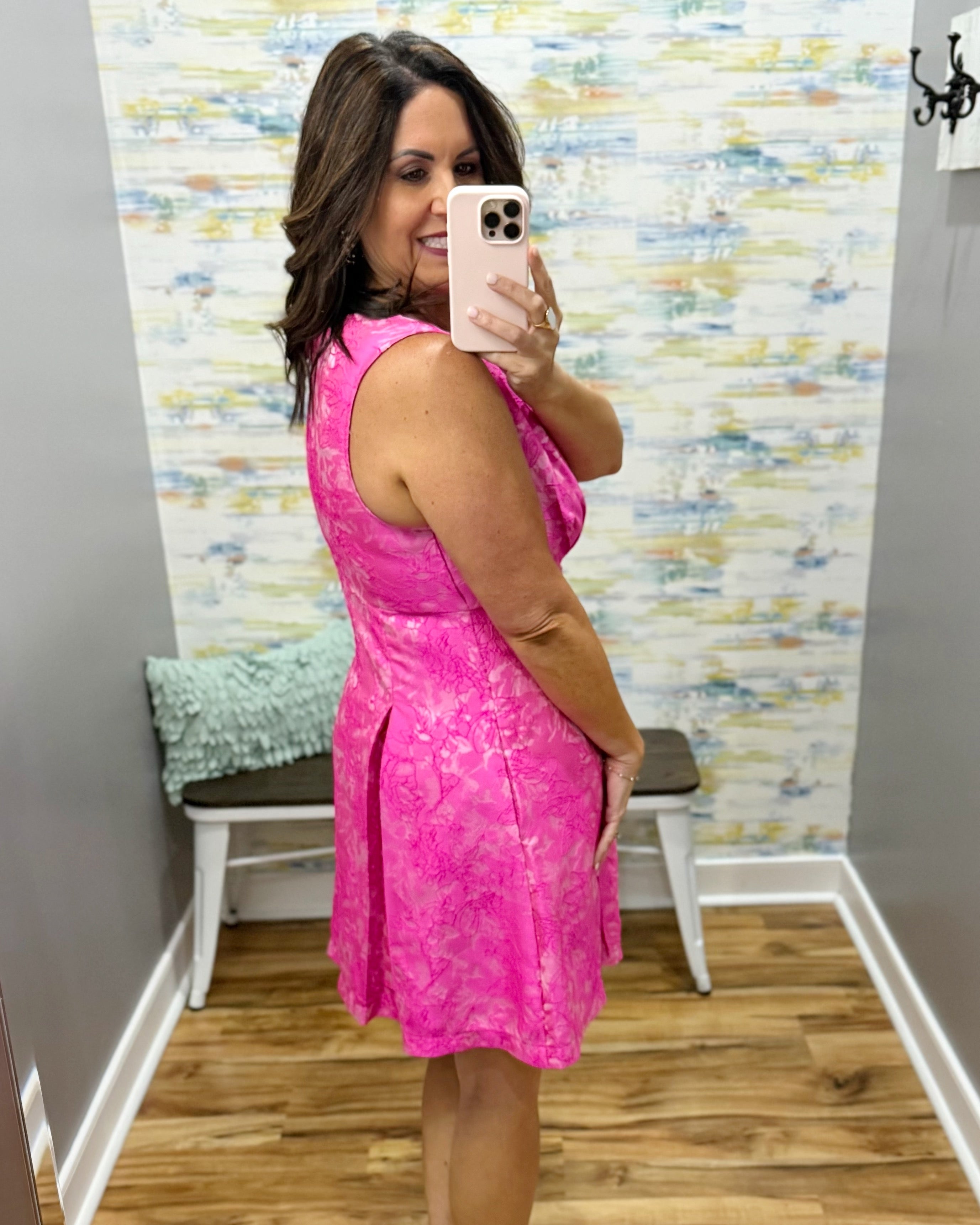 Woman taking a mirror selfie wearing a pink dress in a room with a textured wall.
