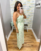 Woman taking a mirror selfie wearing a green floral dress in a room with patterned wallpaper.