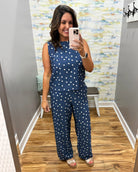 Woman taking a mirror selfie wearing a navy blue outfit with white polka dots in a room with patterned wallpaper.