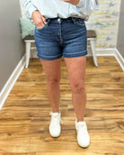 Person wearing blue denim shorts and white sneakers on a wooden floor.