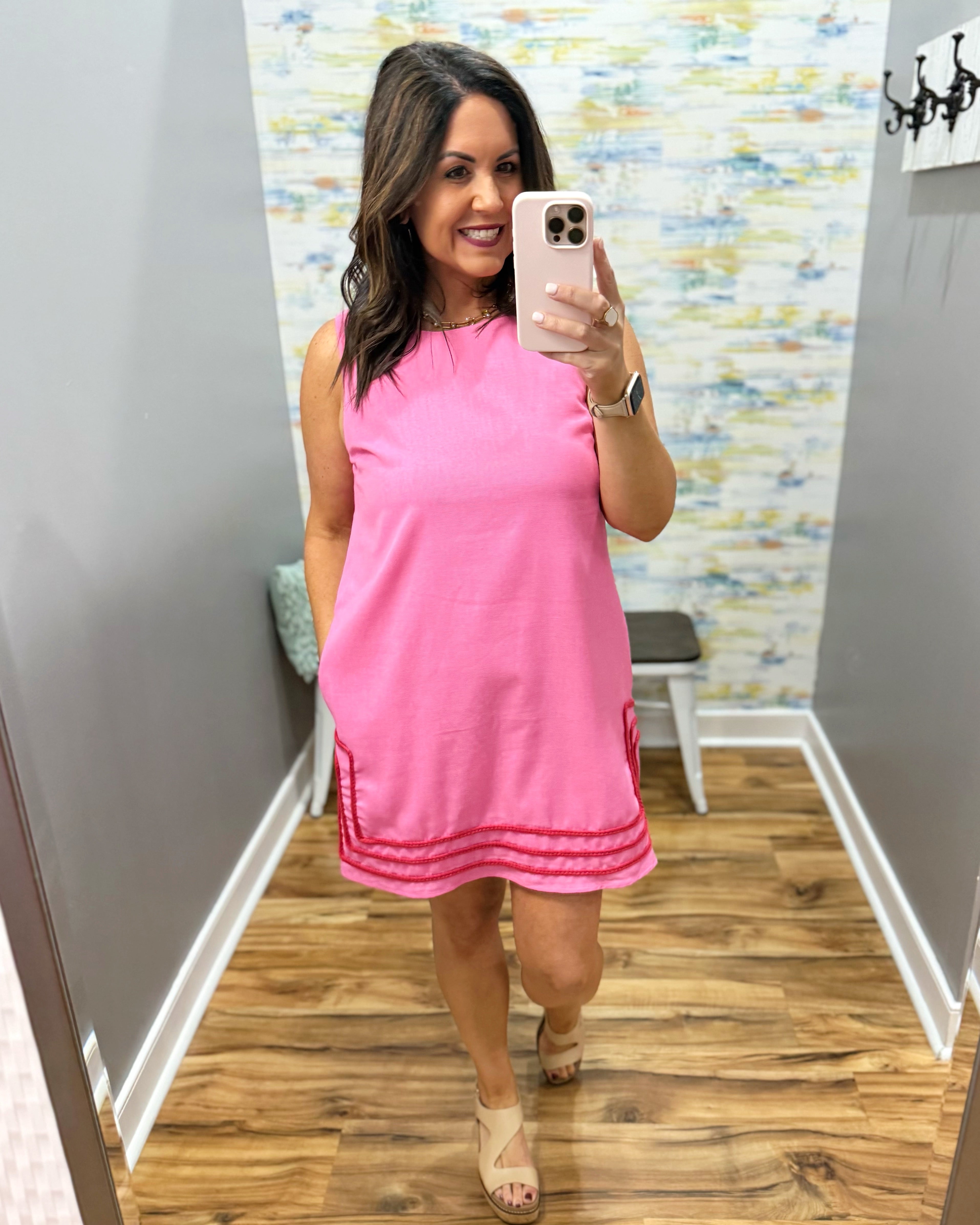 Woman taking a mirror selfie wearing a pink dress in a room with a colorful wall.