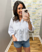 Woman taking a mirror selfie wearing a white striped shirt and denim shorts.