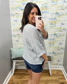 Woman taking a mirror selfie wearing a gray sweater and denim shorts in a room with colorful wall art.