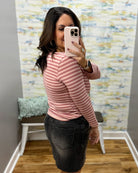 A woman takes a mirror selfie in a fitting room wearing a ginger and mauve striped long-sleeve top and a dark gray denim skirt.