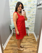 Woman taking a mirror selfie wearing a red dress in a room with a colorful wall.