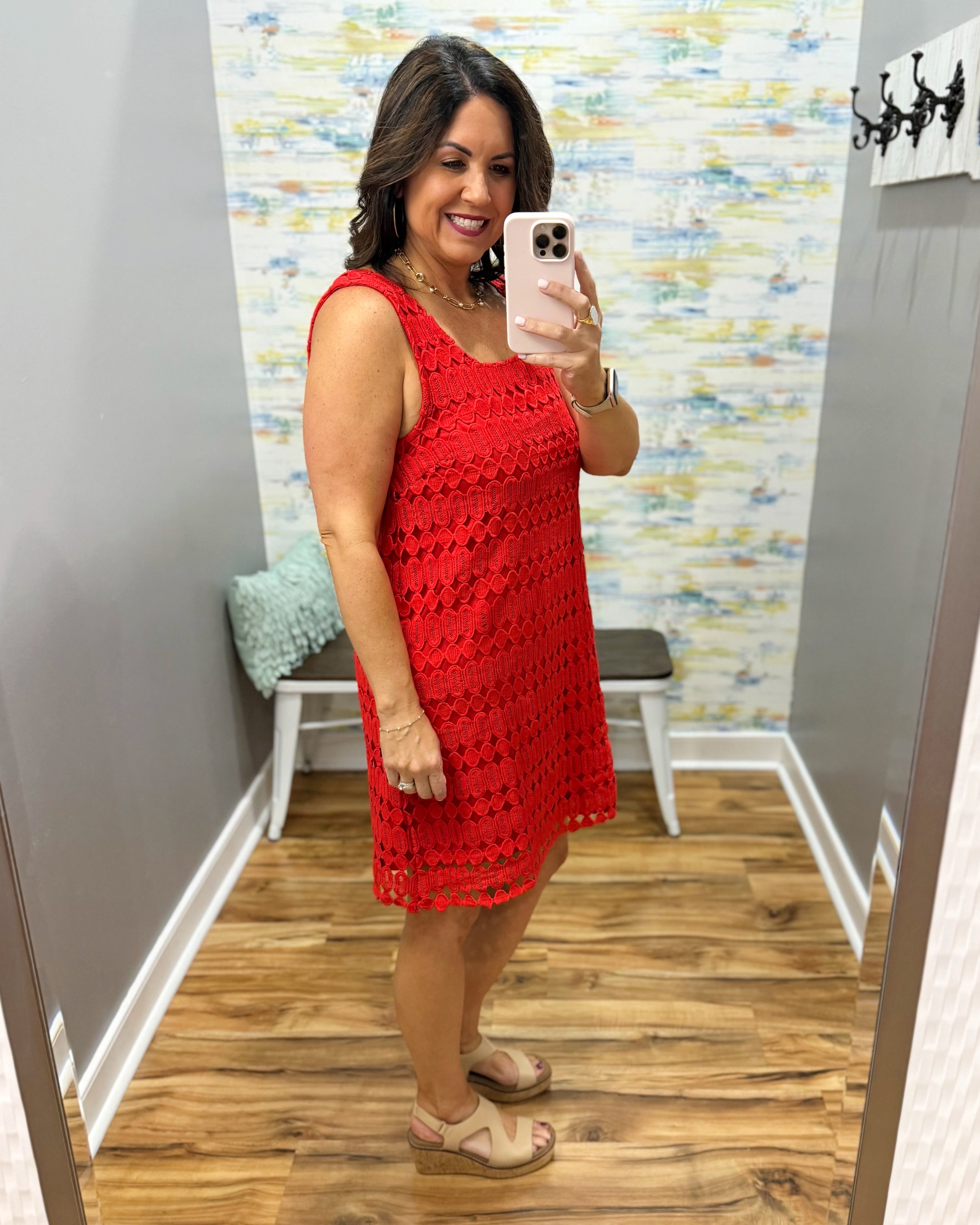 Woman taking a mirror selfie wearing a red dress in a room with a colorful wall.